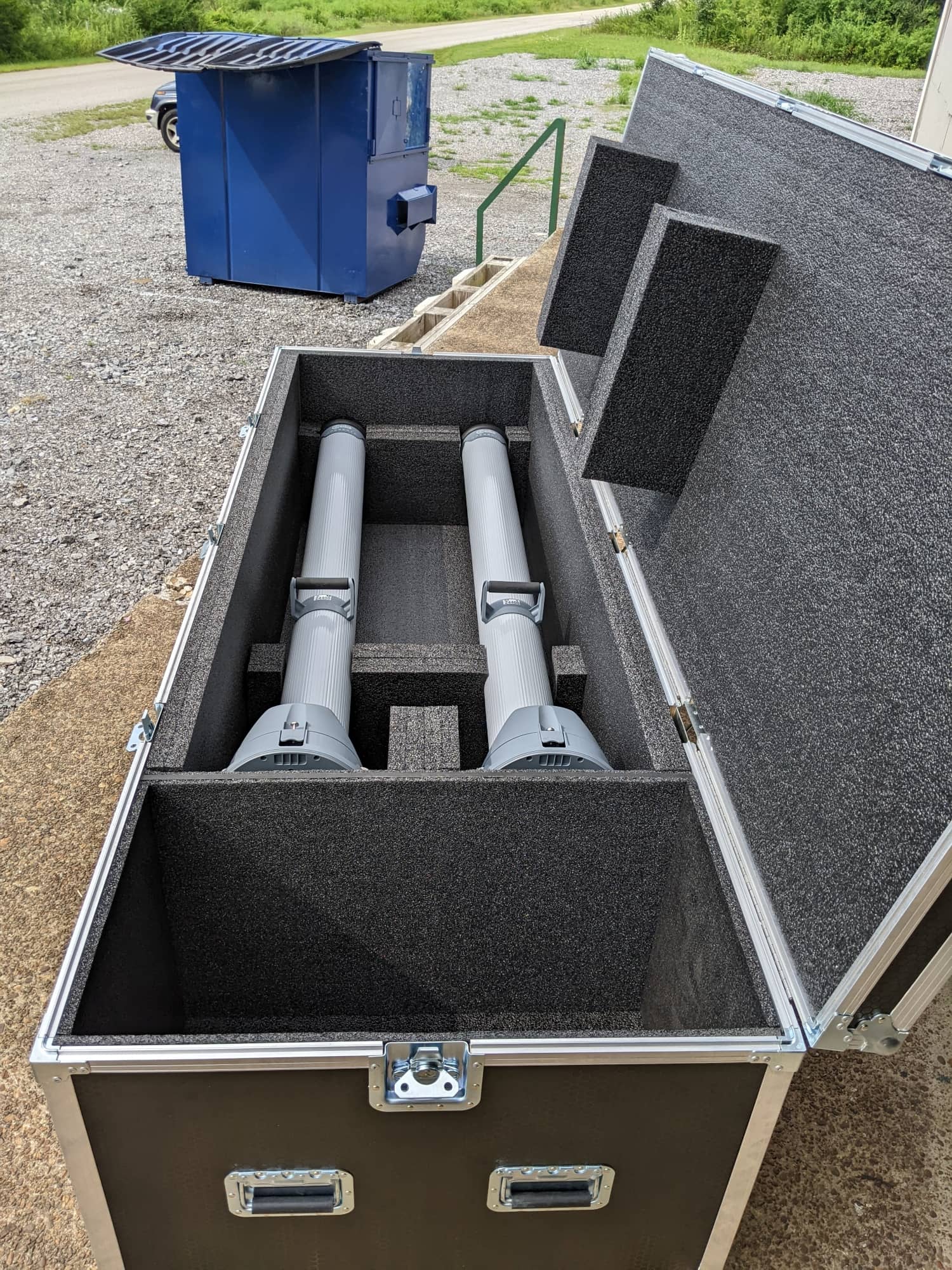 Open foam-lined road case holding two long cylindrical components